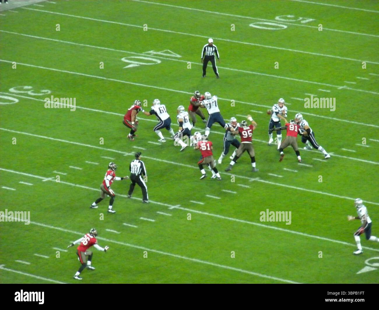 American Football-Spiel in Aktion zwischen zwei Teams auf einem grasbewachsenen Stadionfeld, mit Spielern in rot-weißen Uniformen und Schiedsrichtern Stockfoto