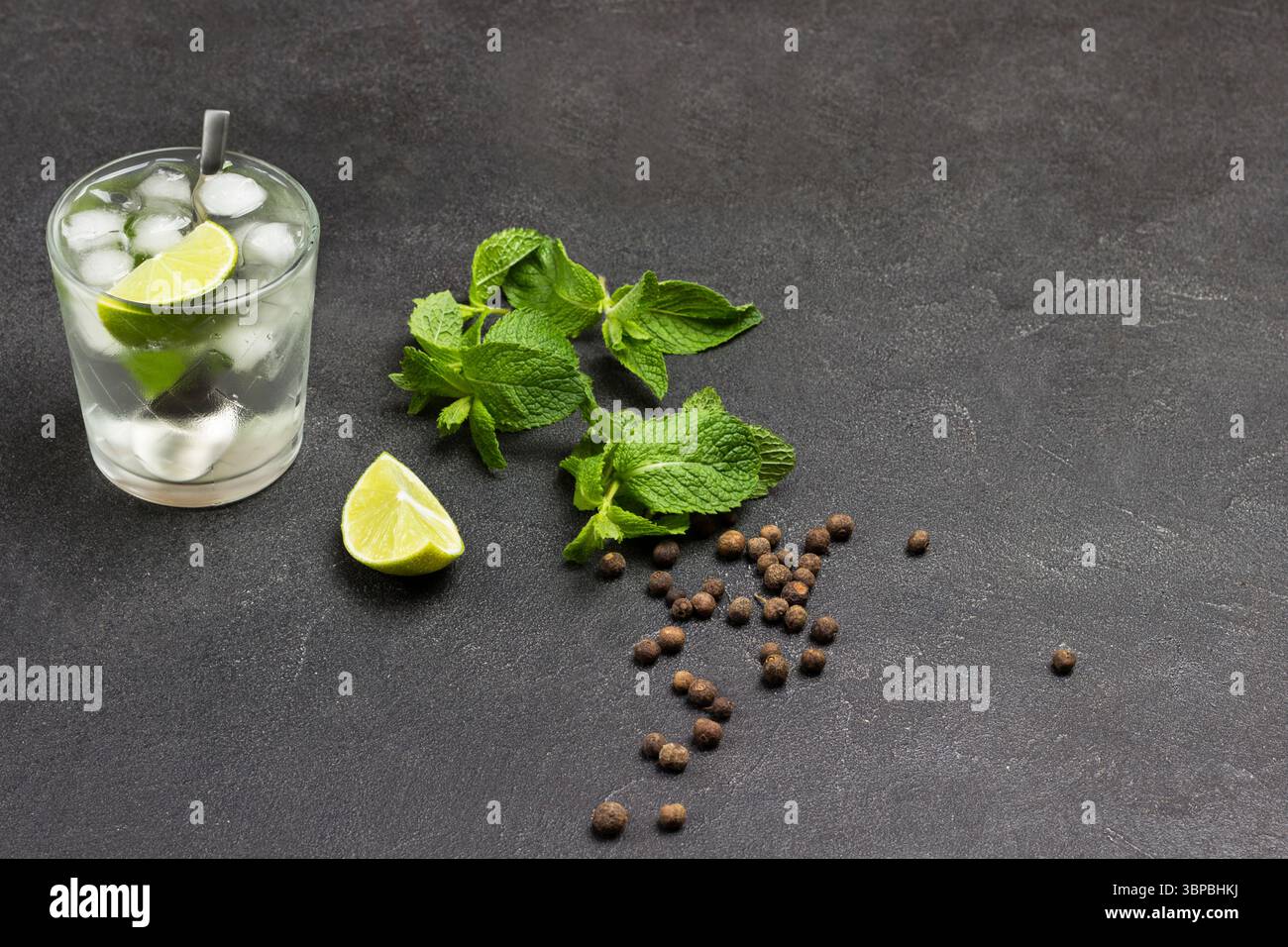 Ein Glas erfrischendes Getränk mit Limette, Minze und Eis. Limettenscheiben und Minzblätter auf dem Tisch. Kopierbereich. Schwarzer Hintergrund. Draufsicht Stockfoto