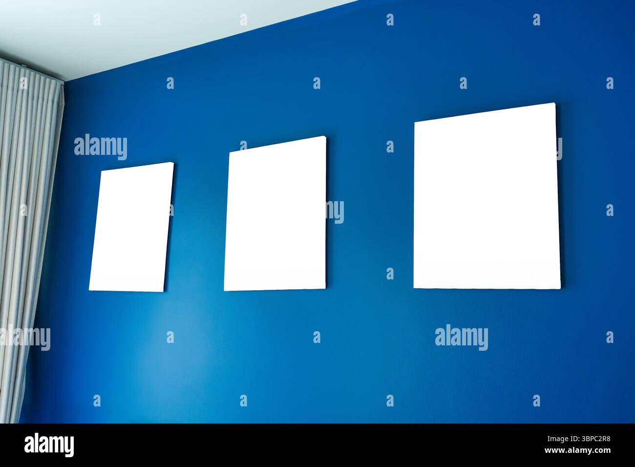 Drei leere, quadratische Leinwandrahmen, die auf einer tiefblauen Wand in einer Eigentumswohnung angeordnet sind. Moderne und minimalistische Ästhetik Stockfoto