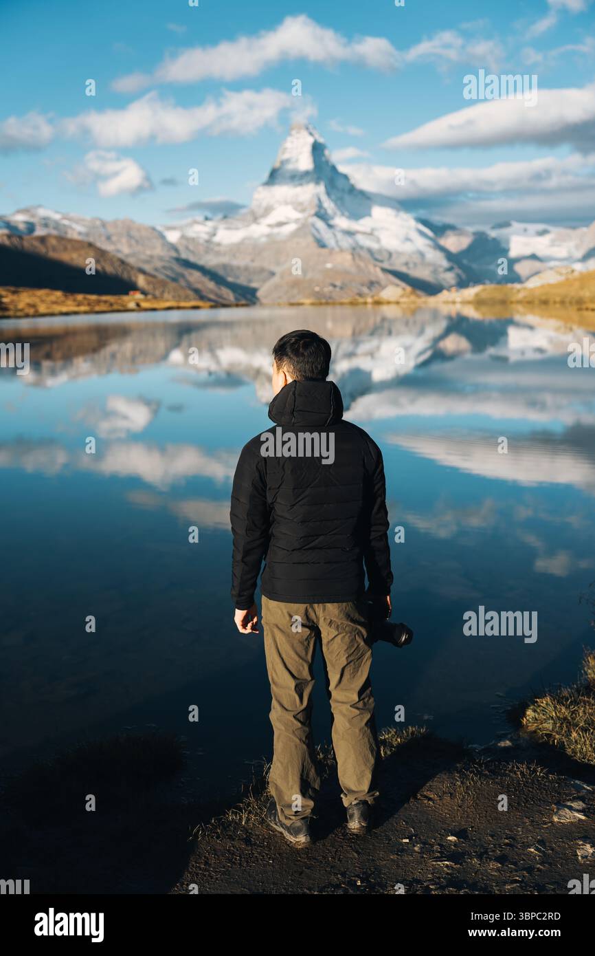 Rückansicht eines Mannes, der eine Kamera am Stellisee hält, mit Matterhorn und blauem Himmel am sonnigen Tag in Zermatt, Schweiz Stockfoto