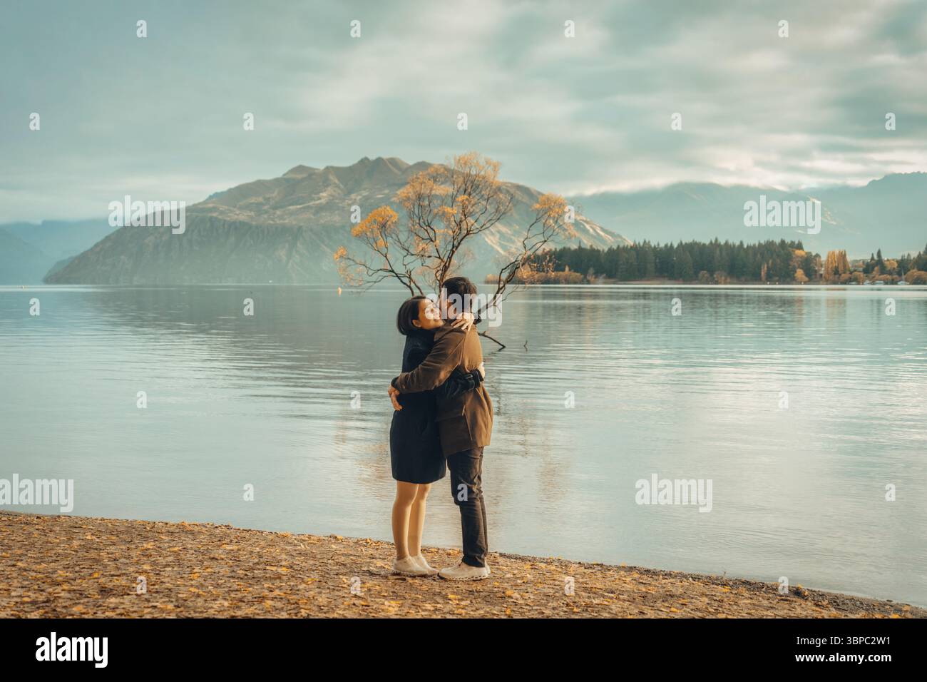 Glückliches asiatisches Paar, das im Herbst in Wanaka, Neuseeland, steht und romantisch mit Willow Tree am Lake Wanaka umgeht Stockfoto