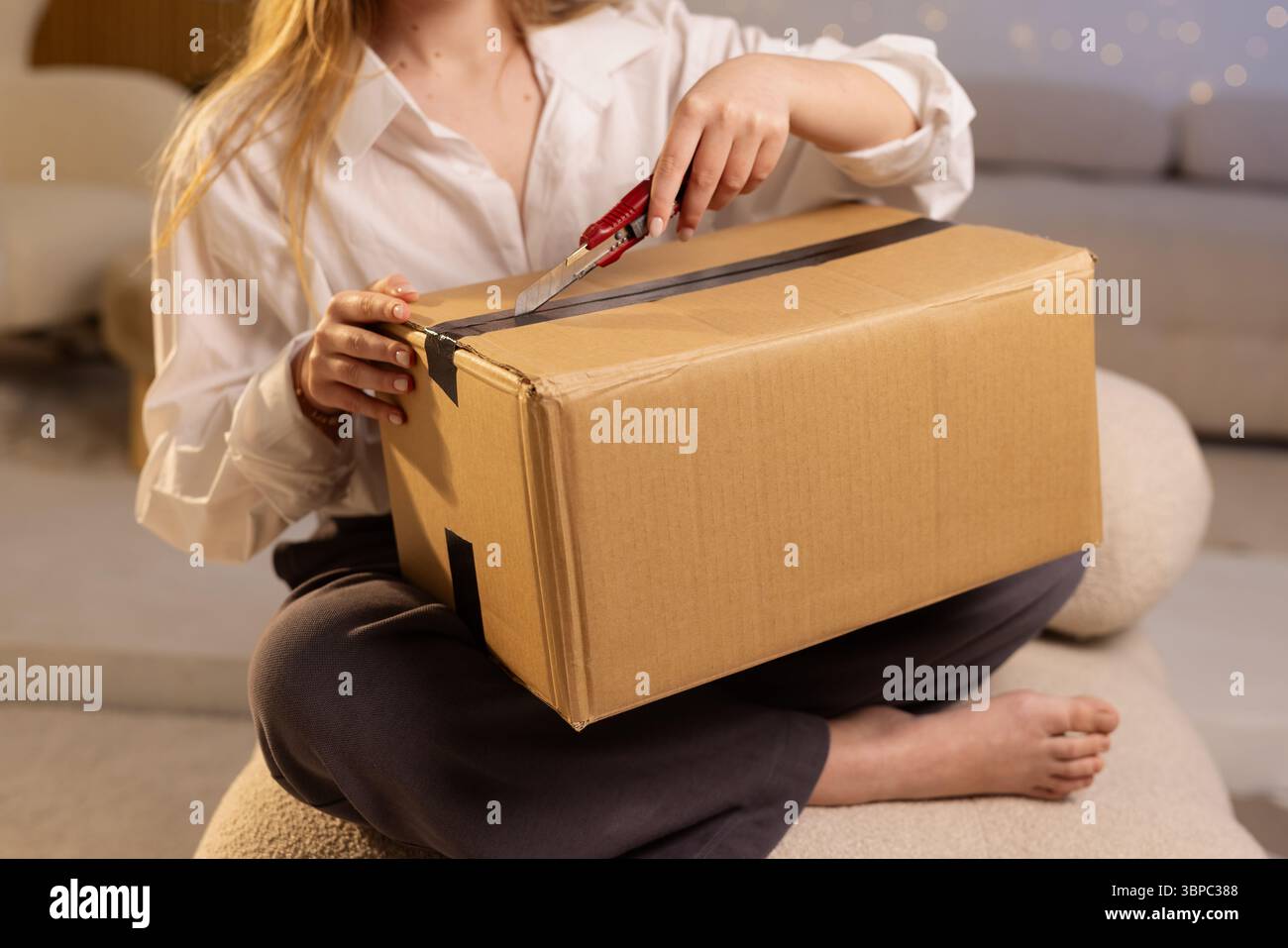 Nahaufnahme einer Frau, die zu Hause ein Paket mit einem Cutter öffnet, die E-Commerce-Zustellung und einen Lifestyle-Moment zeigt Stockfoto