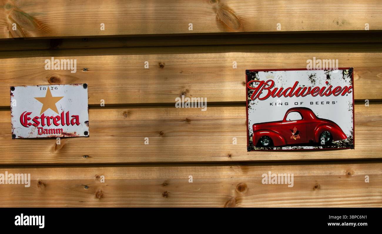 Vintage-Metallschilder für Estrella Damm und Budweiser an einer Holzwand mit klassischem Bier-Branding Stockfoto