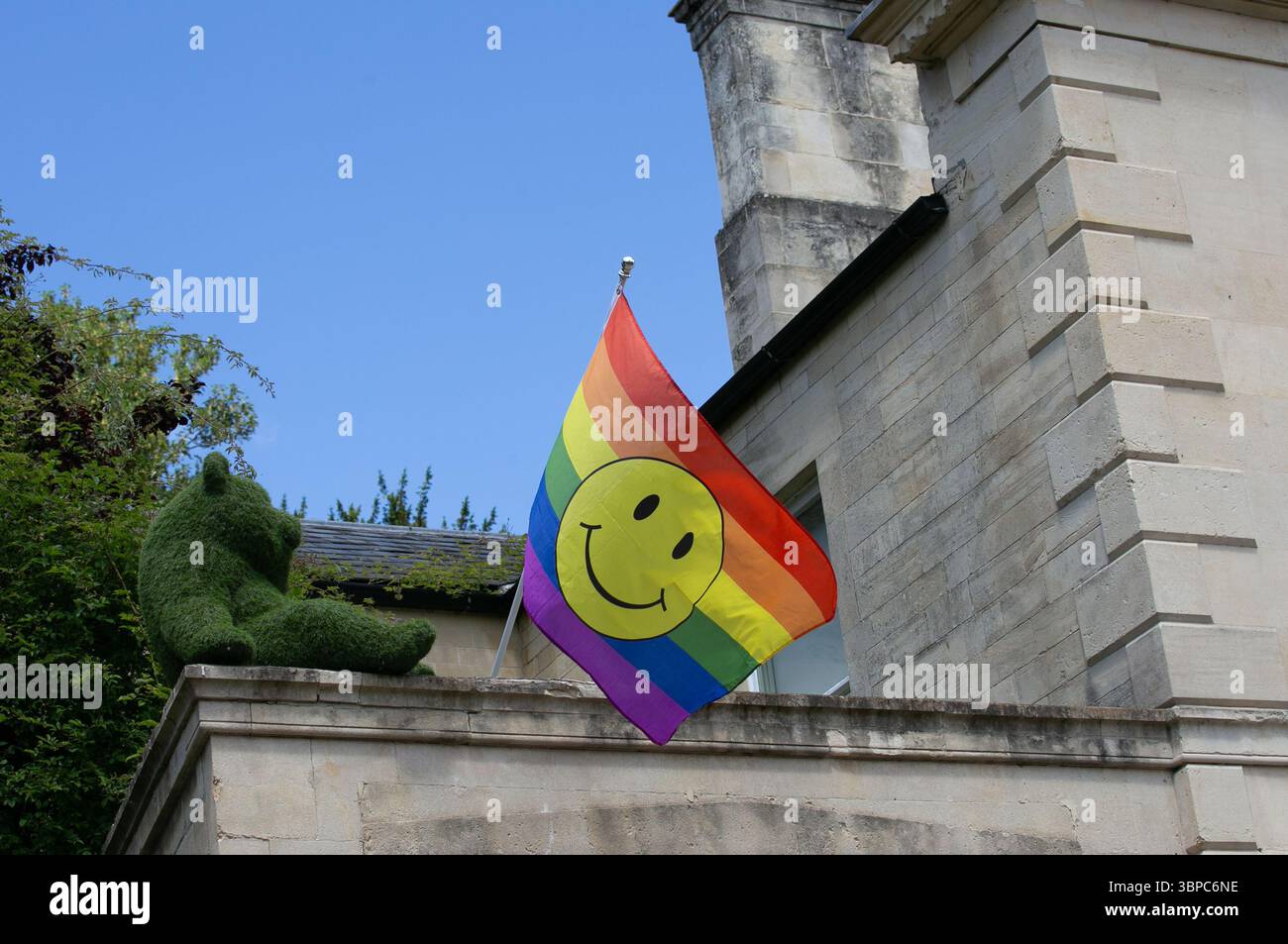 Eine lebhafte Regenbogenfahne mit einem lächelnden Gesicht auf einem Gebäudebalkon in der Nähe einer grünen Formskulptur Bradford auf Avon Wiltshire Stockfoto