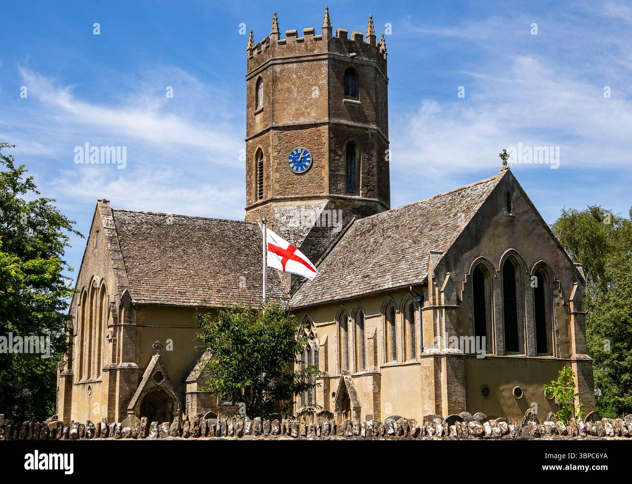 Eine historische englische Kirche von St. Mary's in Uffington Oxfordshire mit einem Steinturm und der Flagge von St. George unter blauem Himmel Stockfoto