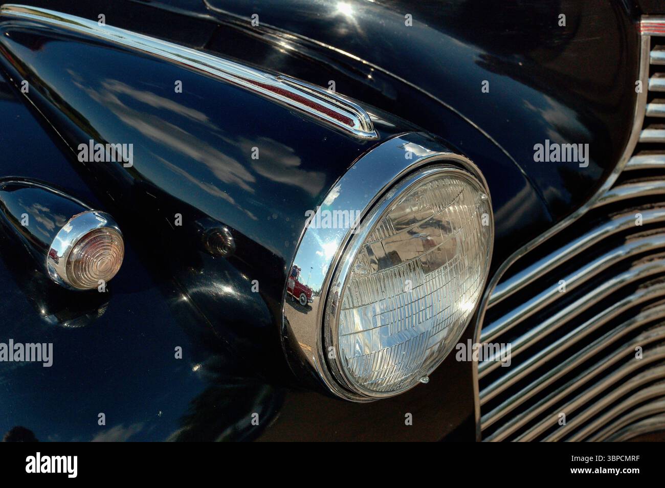 Schließen Sie einen Scheinwerfer und einen Chromgrill an einem schwarzen Oldtimer Stockfoto