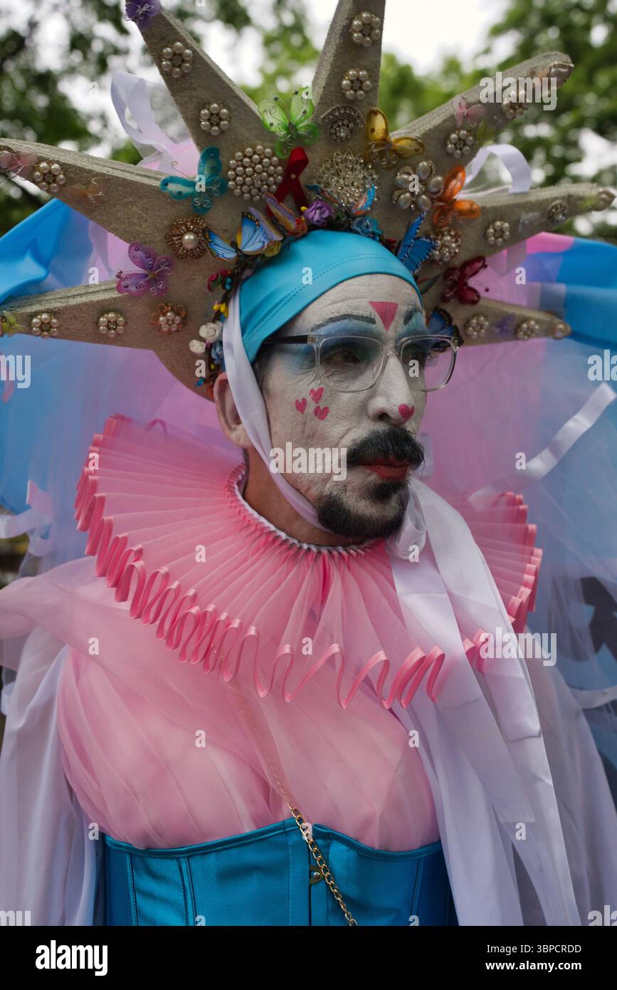 Eine Person in aufwendigem Kostüm mit einem großen sternförmigen Kopfschmuck mit Schmetterlingen und Perlen, einem rosa Rüschenkragen und einem grünen Korsett. Stockfoto