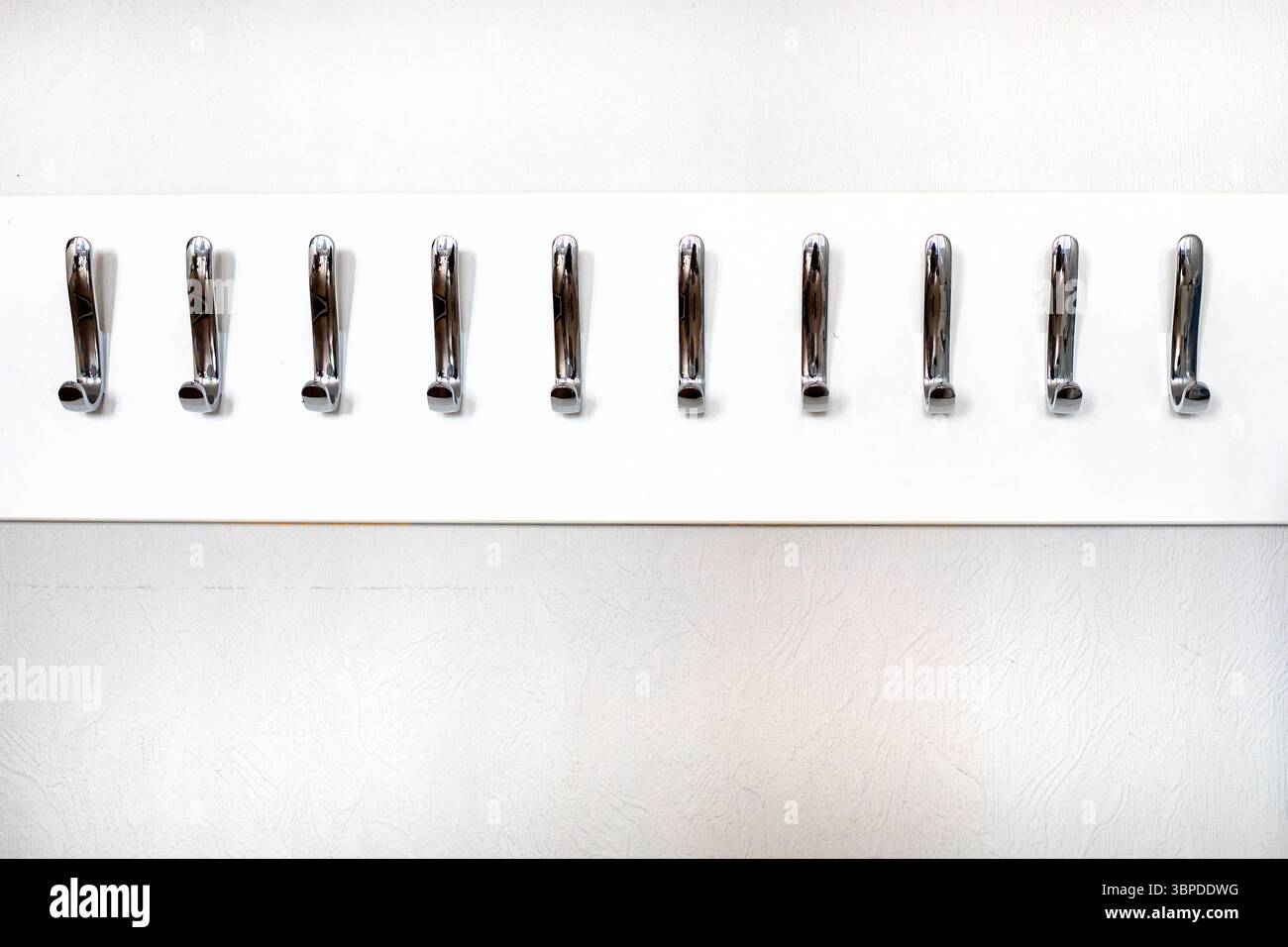 Stilvolle, moderne Metallhaken für Kleidung und Taschen an einer hellen Wand Stockfoto