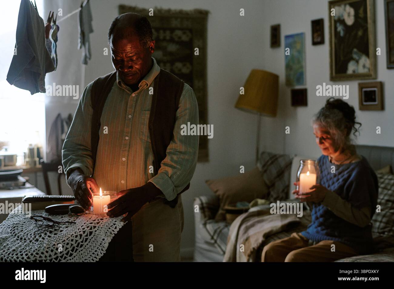 Ältere multiethnische Paare sitzen drinnen und halten Kerzen während der Not Stockfoto