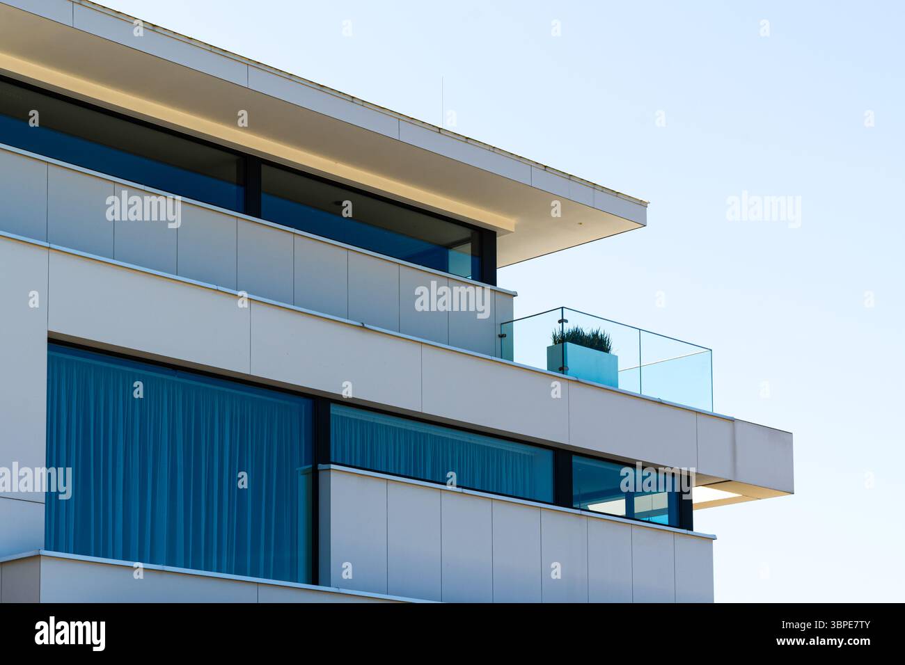 Modernes weißes Apartmentgebäude mit klaren Linien, Glasgeländern und minimalistischer Ästhetik Stockfoto