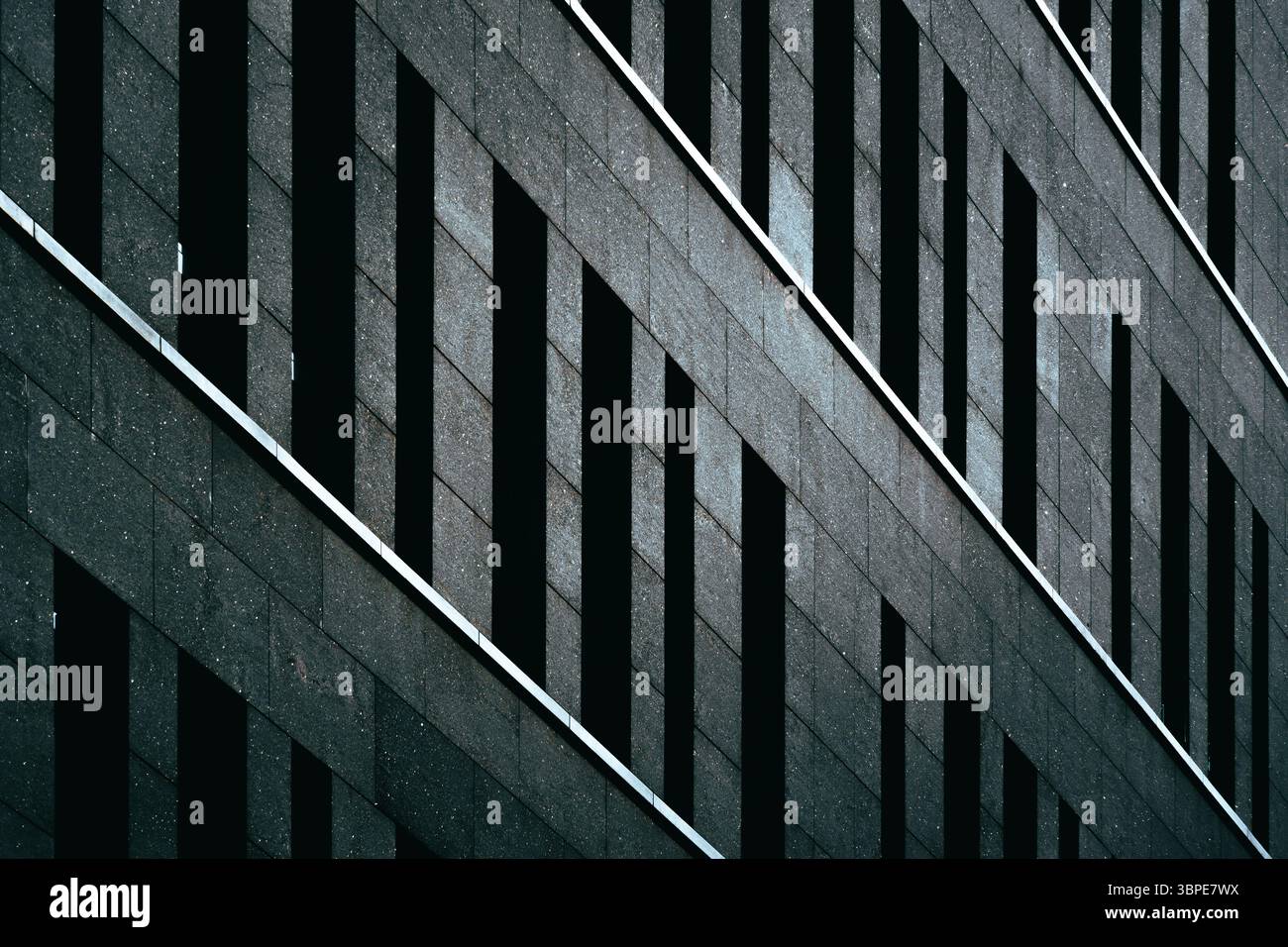 Monolithisches dunkles Gebäude mit vertikalen Schlitzen, die einen dramatischen Rhythmus über die Steinfläche erzeugen Stockfoto