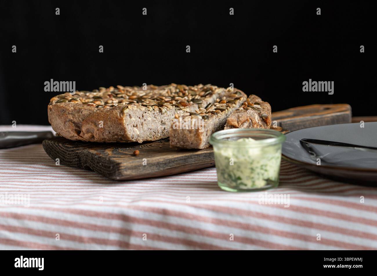 Frisches, hausgemachtes grünes Buchweizenbrot im Multikocher gebacken, in Scheiben geschnitten und auf Holzbrett mit Kräuterbutter-Aufstrich serviert, gesunde glutenfreie Backcreme Stockfoto