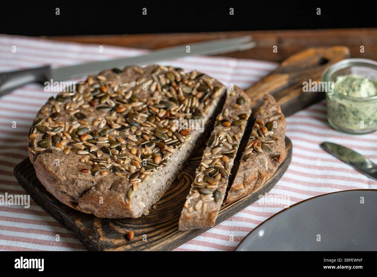 Frisches, hausgemachtes grünes Buchweizenbrot im Multikocher gebacken, in Scheiben geschnitten und auf Holzbrett mit Kräuterbutter-Aufstrich serviert, gesunde glutenfreie Backcreme Stockfoto