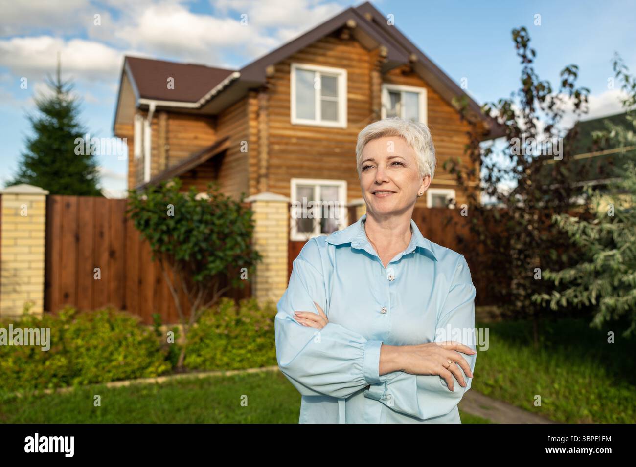 Eine selbstbewusste Frau, die stolz vor einem gemütlichen, einladenden Zuhause steht, das sie liebt Stockfoto