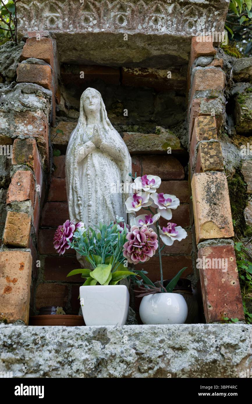 Kleiner Schrein mit Marienfigur in Nische aus Ziegeln und Steinen, dekoriert mit Blumen auf der Insel Torcello, Italien. Stockfoto