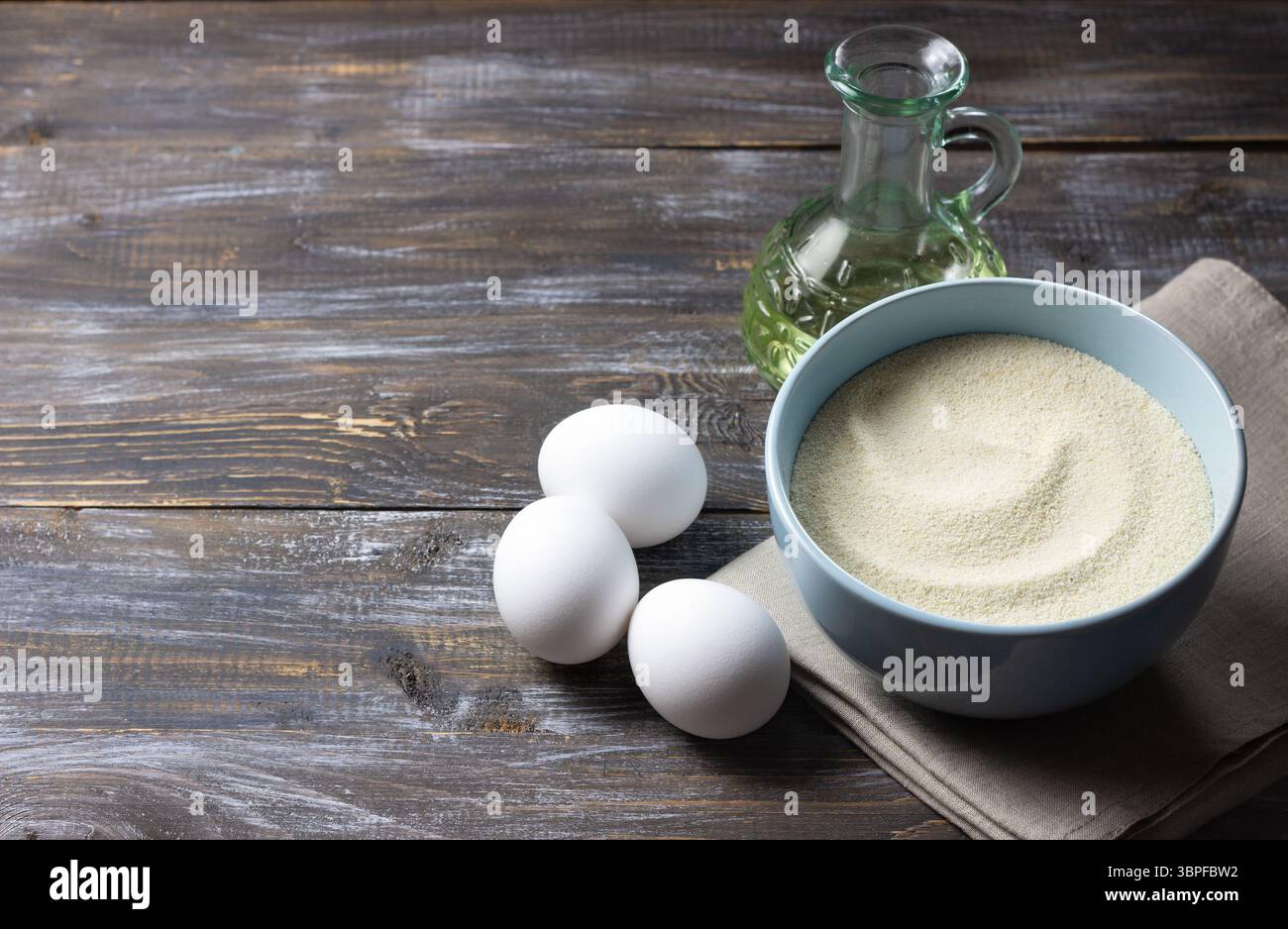 Grieß in der Schüssel, Eier und Pflanzenöl auf rustikalem Holztisch, Zutaten zum hausgemachten Kochen und Backen Stockfoto