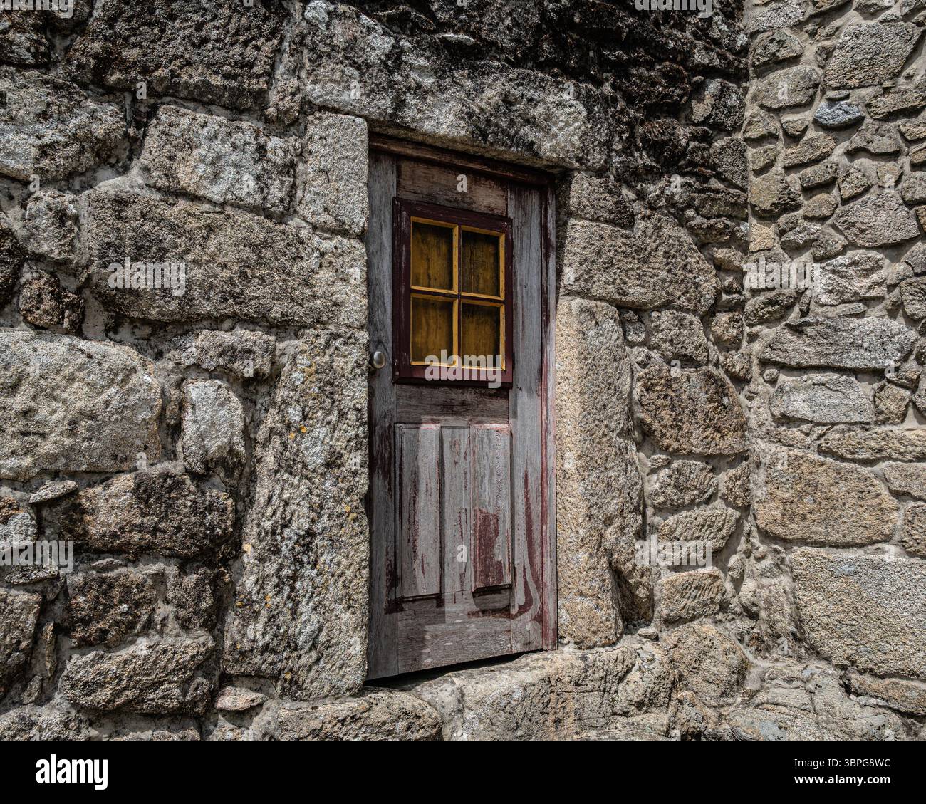 Alte, abgenutzte Tür und ein typisches gelb gerahmtes Fenster, das in eine Steinmauer einer Wohnung in Sistelo, Portugal, eingebaut ist. Stockfoto
