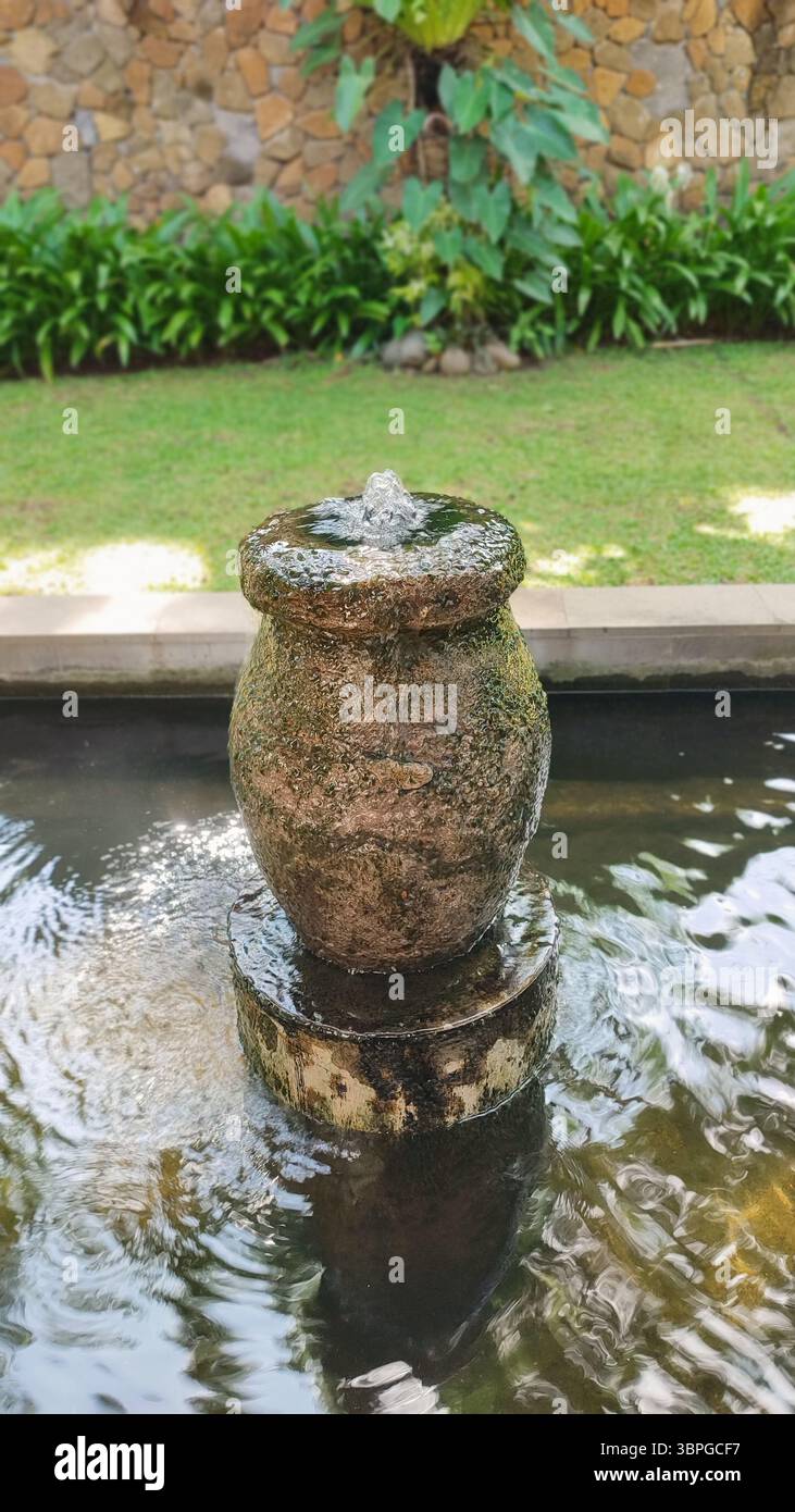 Steintopf-Wasserbrunnen in einem ruhigen Gartenteich schaffen eine friedliche und entspannende Atmosphäre im Freien. - Smartphone-aufgenommenes Stockfoto