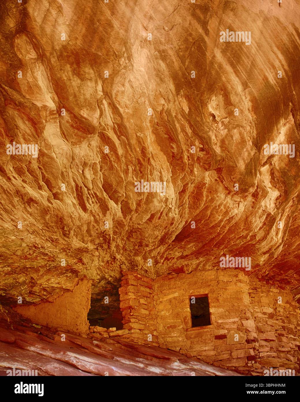 Haus auf der Feuerruine, alte alte Puebloan-Speicher unter einem leuchtend roten Sandsteinüberhang im Mule Canyon, nahe Blanding, Utah, USA. Stockfoto