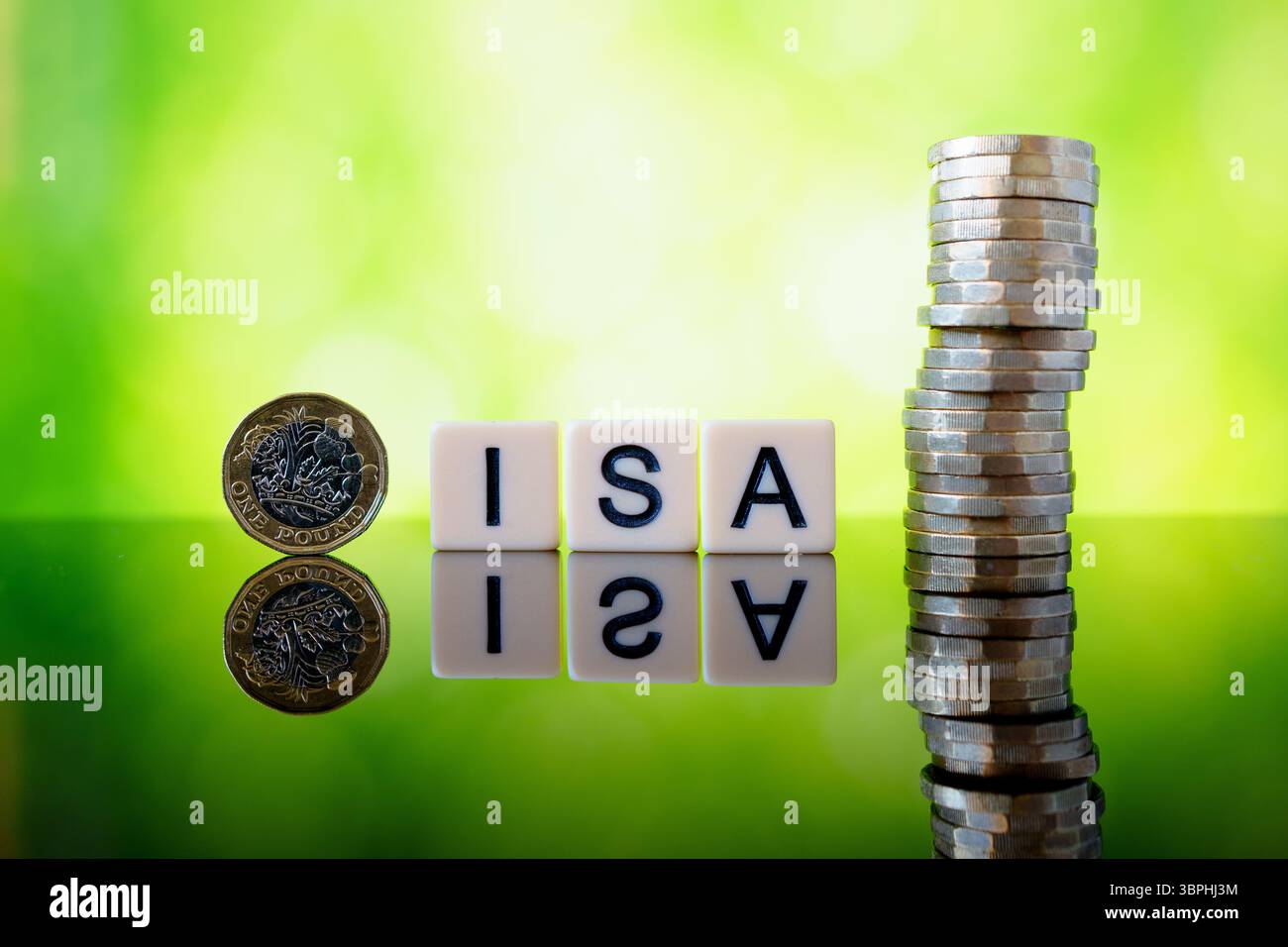 ISA steuerfreies Sparkonzept mit Buchstabensteinen, einem Pfund-Münze und einem hohen Stapel Sterling-Münzen, die auf glänzender Oberfläche gegen grünes Bokeh bac reflektiert werden Stockfoto