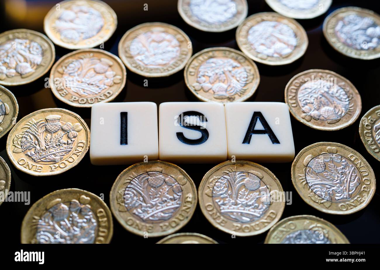 Individuelles Sparkonto. Makroansicht von ISA-Würfeln in verstreuten Pfund-Münzen, die ein Geldmuster bilden, das steuerfreie Einsparungen in Großbritannien hervorhebt. Stockfoto