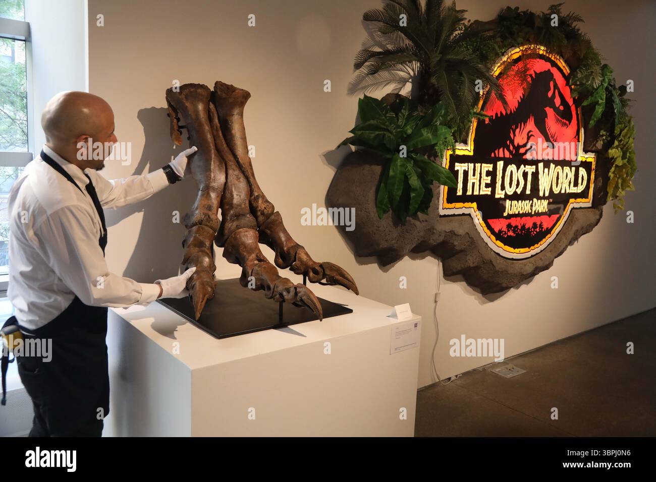 New York, New York, USA. Juli 2025. Ein Handler, der mit einem beweglichen Tyrannosaurus Rex Foot in der späten Kreidezeit (vor ca. 67 Millionen Jahren), Hell Creek Formation, Garfield Co., Montana, geschätzte 250.000 - 350.000, und The Lost World: Jurassic Park (1997) Original LED Sign aus SEGA's The Lost World: Jurassic Park Light Gun Arcade Game, ca. 1997 Schätzung 20.000 - 30.000, zu sehen in der Pressevorschau der Geek Week 2025 in Sotheby's New York. (Kreditbild: © Nancy Kaszerman/ZUMA Press Wire) NUR REDAKTIONELLE VERWENDUNG! Nicht für kommerzielle ZWECKE! Stockfoto