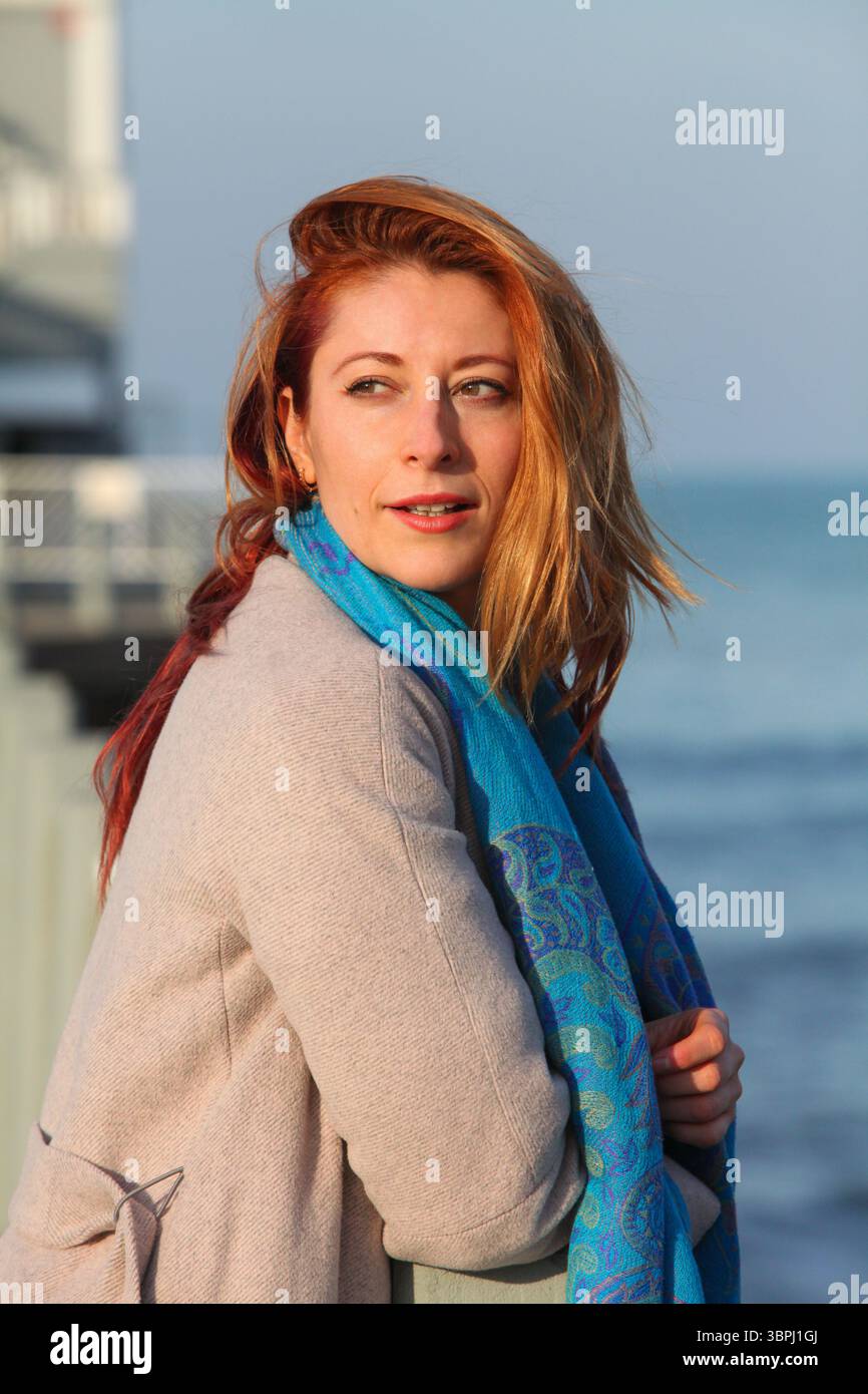 Nahaufnahme einer rothaarigen Frau in Herbstkleidung, die draußen auf dem Pier steht, verloren in Gedanken. Stockfoto