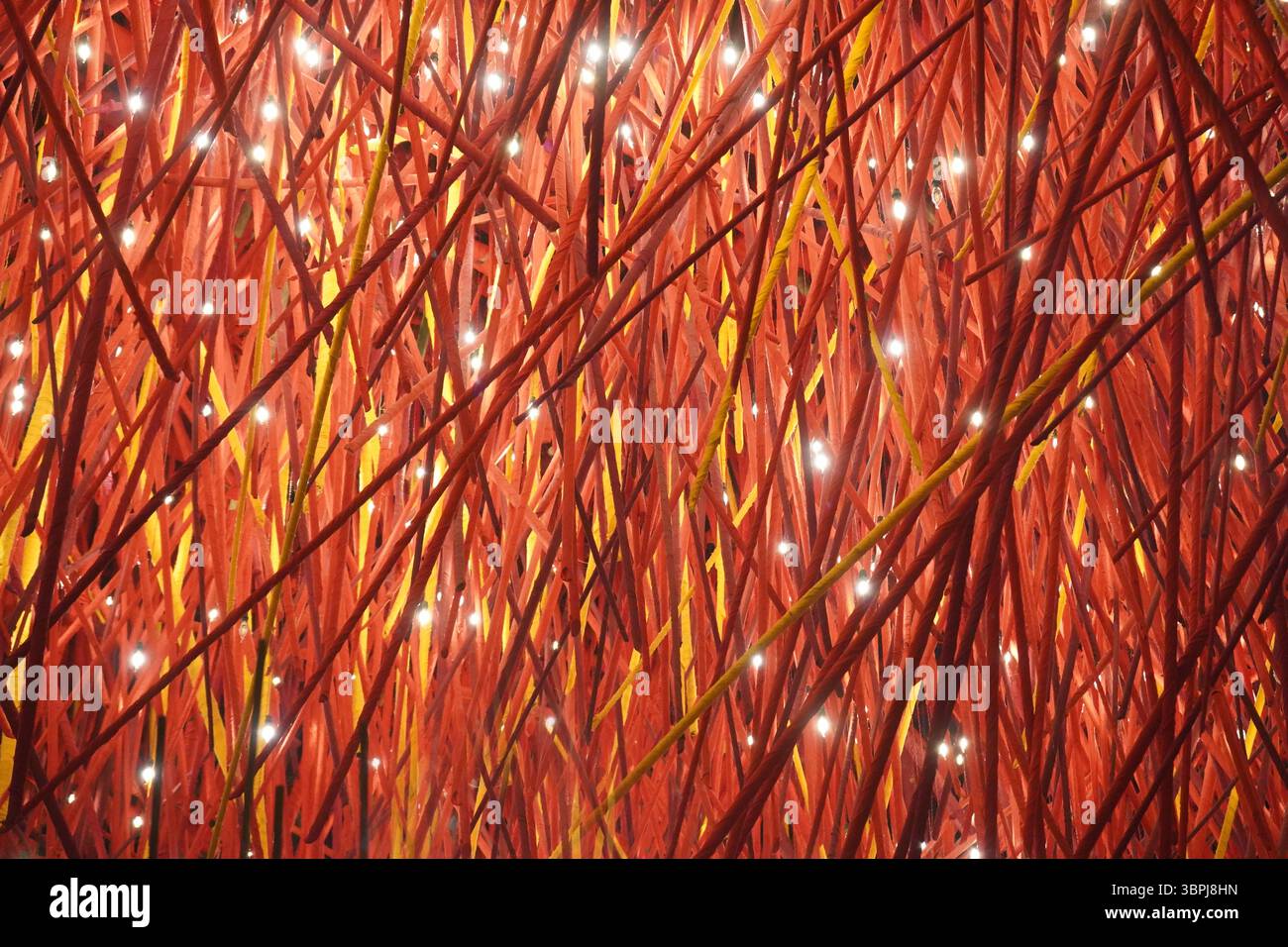 Abstrakte Installation von ineinander verwobenen roten Sticks mit eingebetteten festlichen Lichtern Stockfoto