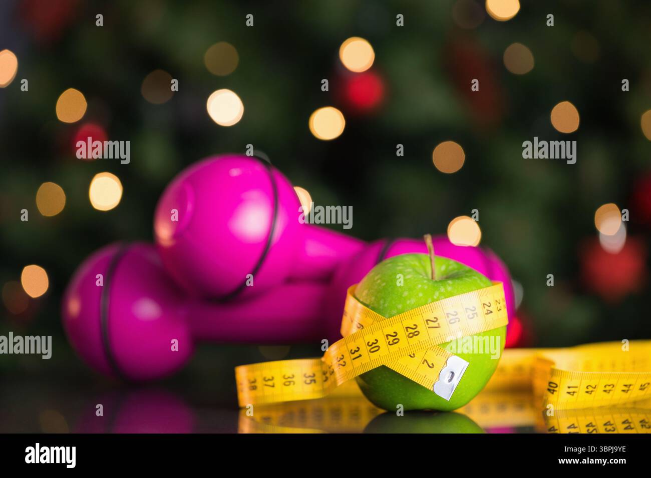 Grüner Apfel sitzt in Klebeband auf der Tischplatte mit rosa Kurzhanteln, Bokeh in flachem Design Stockfoto