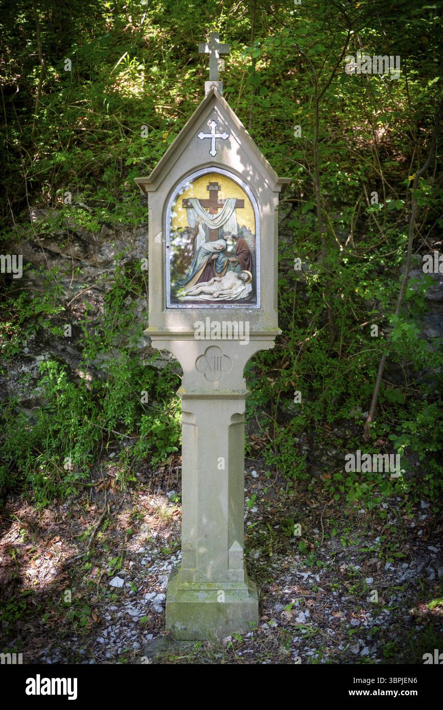 Ein Wegeskreuz oder ein Schrein am Wegesrand mit christlichen Szenen aus dem Leben Christi hinter Glas auf einem Waldweg im Licht der Sonne Stockfoto