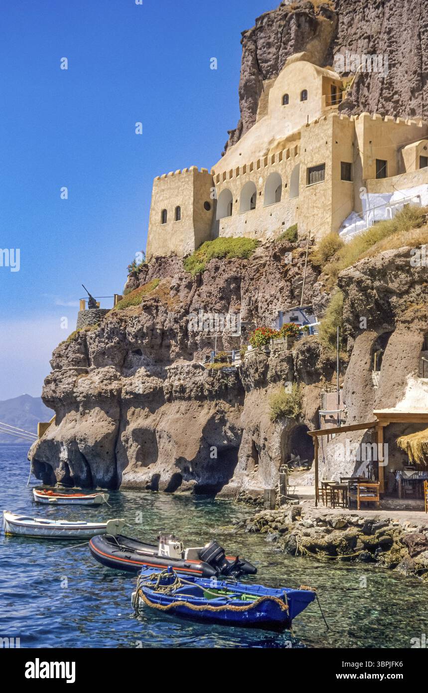 Ein in den Felsen der Klippe im Krater der Insel San Turin im östlichen Mittelmeer gebautes Haus mit verschiedenen Ruderbooten und Motorbooten anc Stockfoto