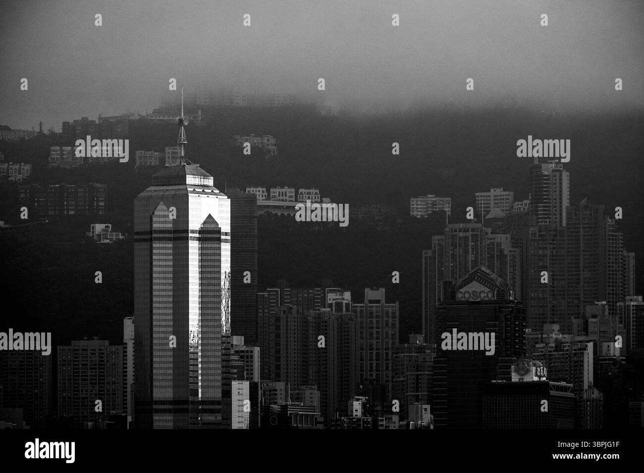Das Gewerbegebiet von Hongkong mit einer Mischung aus modernen Wolkenkratzern und nebeligen Hügeln im Hintergrund, die in Schwarz-weiß erfasst werden. Stockfoto