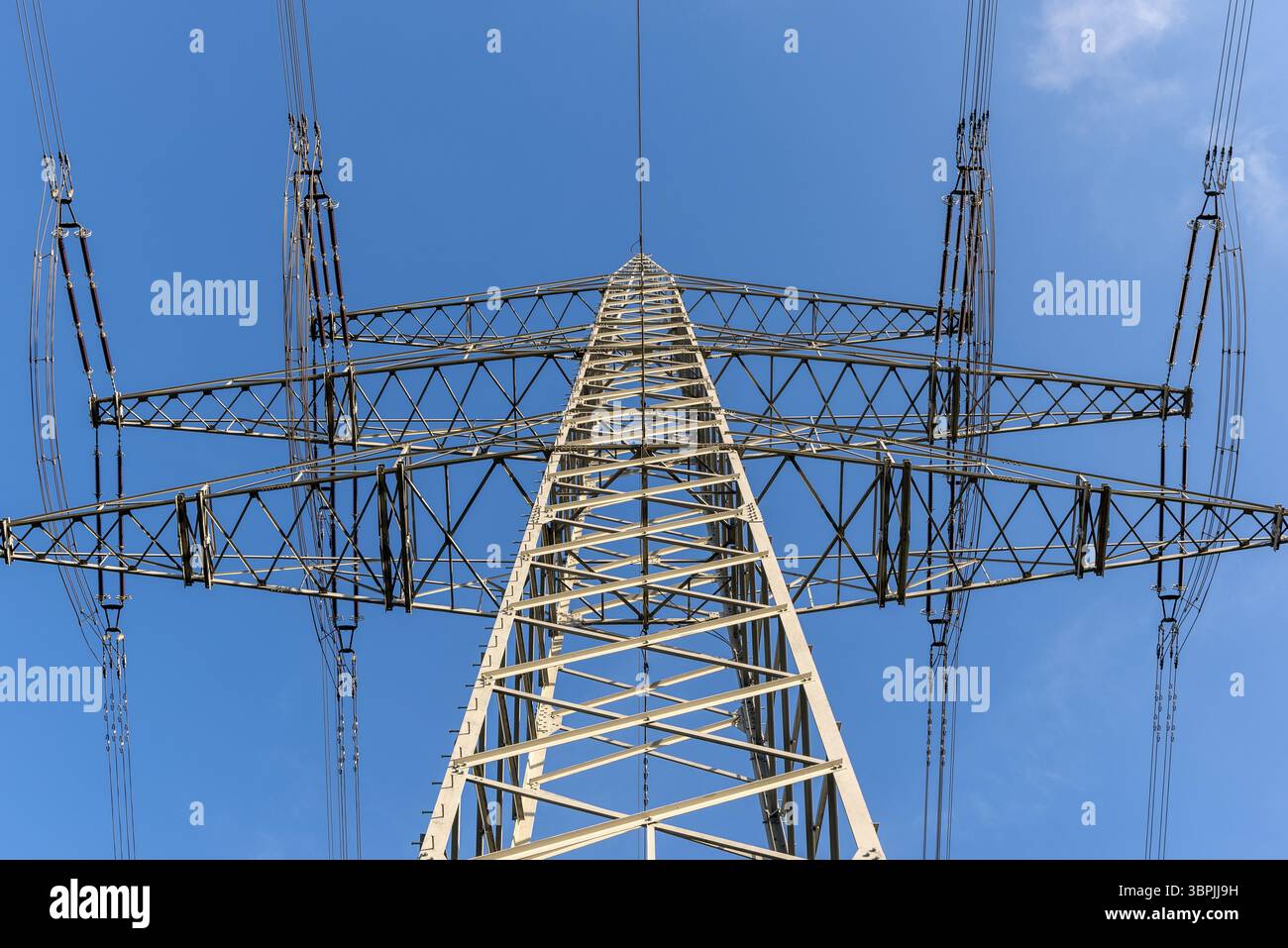 Die Streben, Isolatoren und Kabel des Pylons einer Hochspannungs- oder Freileitung von unten gesehen gegen eine blaue, fast wolkenlose SK Stockfoto