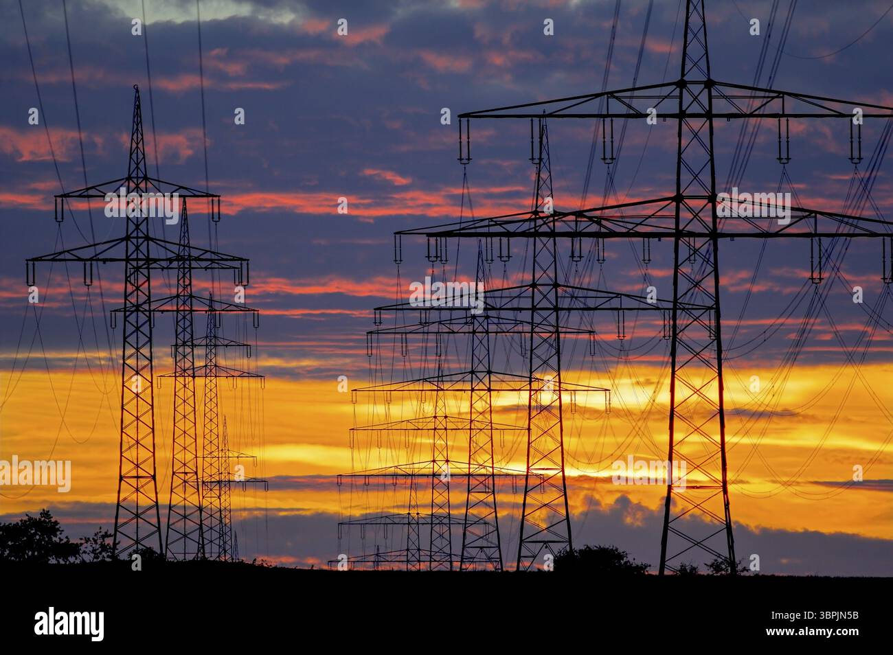 Strommasten und Freileitungen vor einem stimmungsvollen Abendhimmel, hinterleuchtet vom Nachglühen der untergehenden Sonne am Horizont, Frankfu Stockfoto
