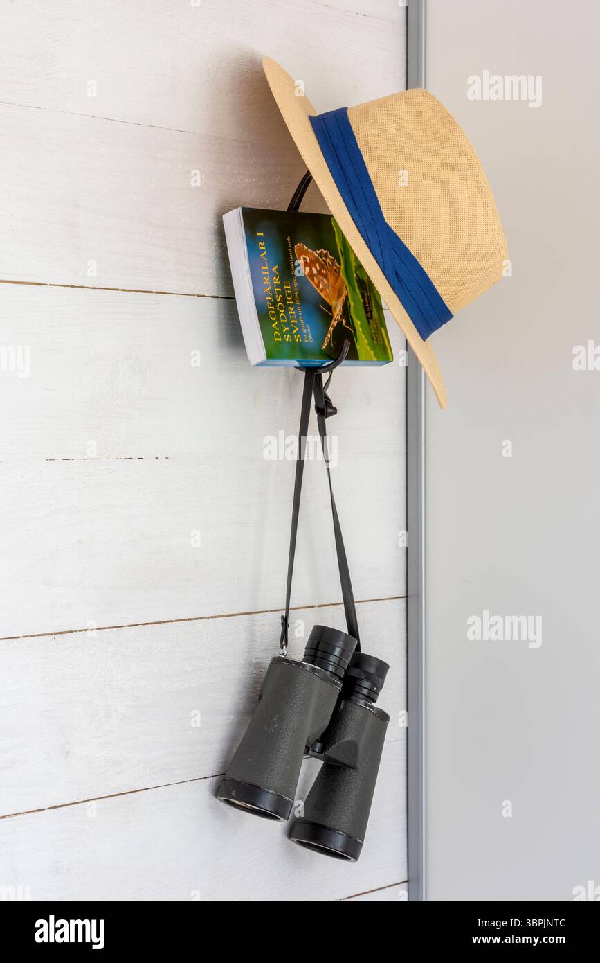 Ein Hut, ein Buch über Schmetterlinge und Ferngläser, die an einem Haken an der Wand hängen Stockfoto