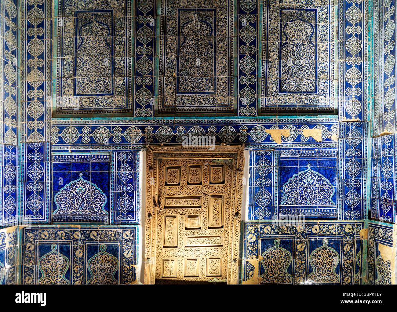 Eine wunderschön dekorierte Wand mit komplexen blauen Fliesen und kunstvollen Mustern, mit einer Holztür in der Mitte. Das Design zeigt ein traditionelles cr Stockfoto