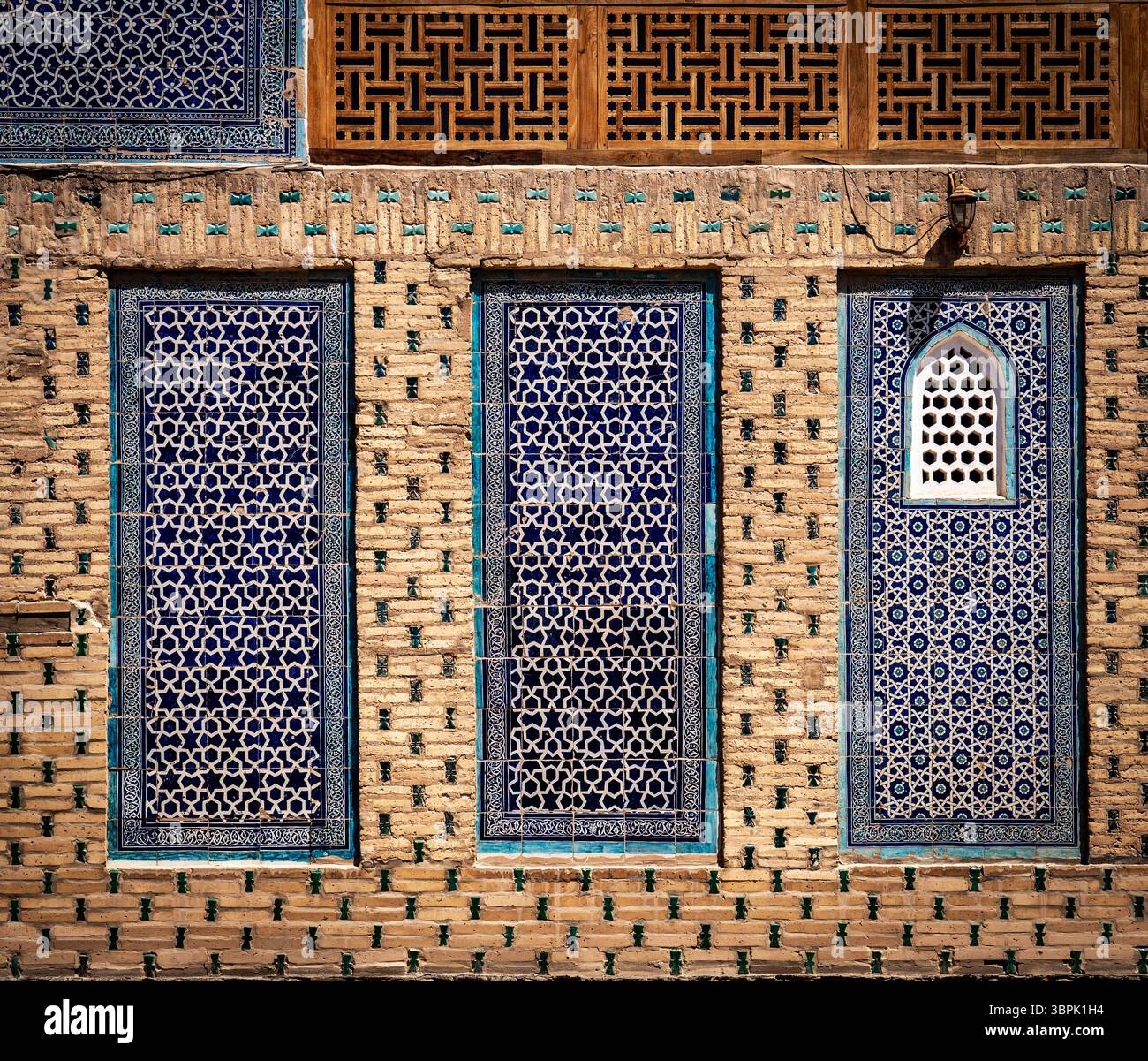 Nahaufnahme einer dekorativen Wand mit komplexen blauen Fliesen und geometrischen Mustern. Die Wand zeigt jeweils drei unterschiedliche Fensterdesigns Stockfoto