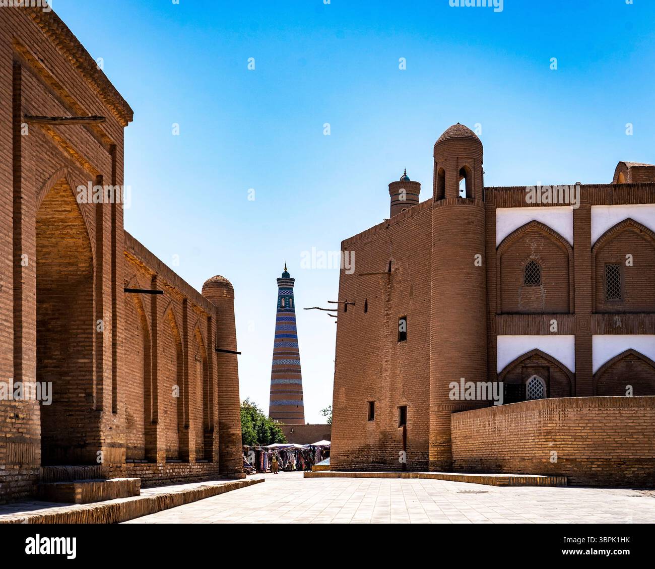 Ein malerischer Blick auf die antike Architektur in einer historischen Stadt, mit Backsteinhäusern und einem hohen Minarett im Hintergrund unter einem klaren blauen Himmel Stockfoto