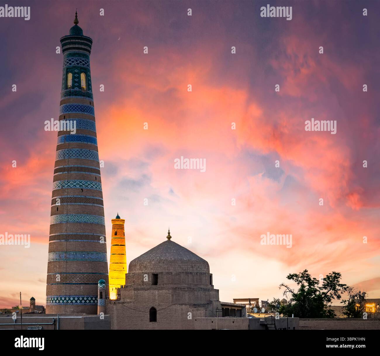 Ein atemberaubender Blick auf die antike Architektur mit einem hohen Minarett und einer Kuppelstruktur vor einem lebendigen Sonnenuntergang. Die Szene fängt komplizierte Patte ein Stockfoto