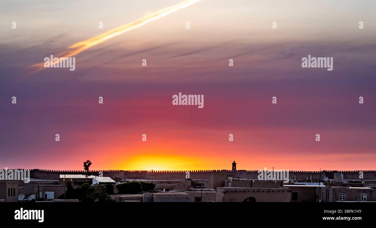 Ein atemberaubender Blick auf den Sonnenuntergang über eine Stadtlandschaft mit Silhouetten von Gebäuden und einer Mauer. Der Himmel ist in leuchtenden Orange-, Lila- und Rosa-Tönen gemalt Stockfoto