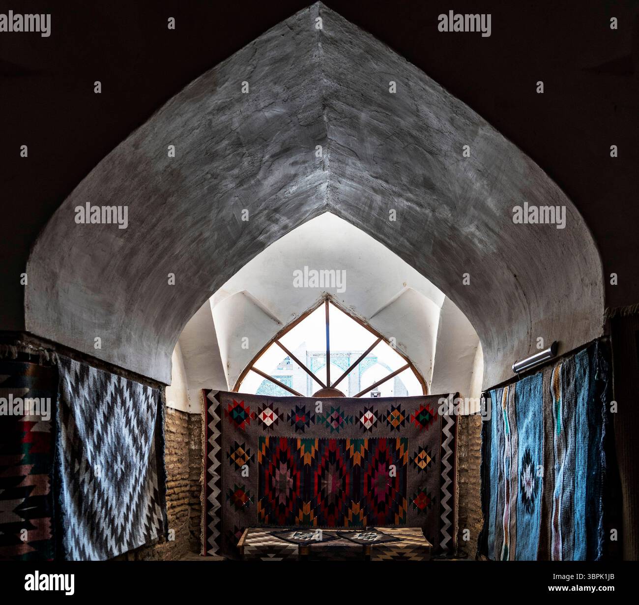 Ein wunderschön gestaltetes Interieur mit bogenförmiger Architektur und farbenfrohen Teppichen, die an den Wänden hängen. Das Licht filtert durch eine große Stockfoto