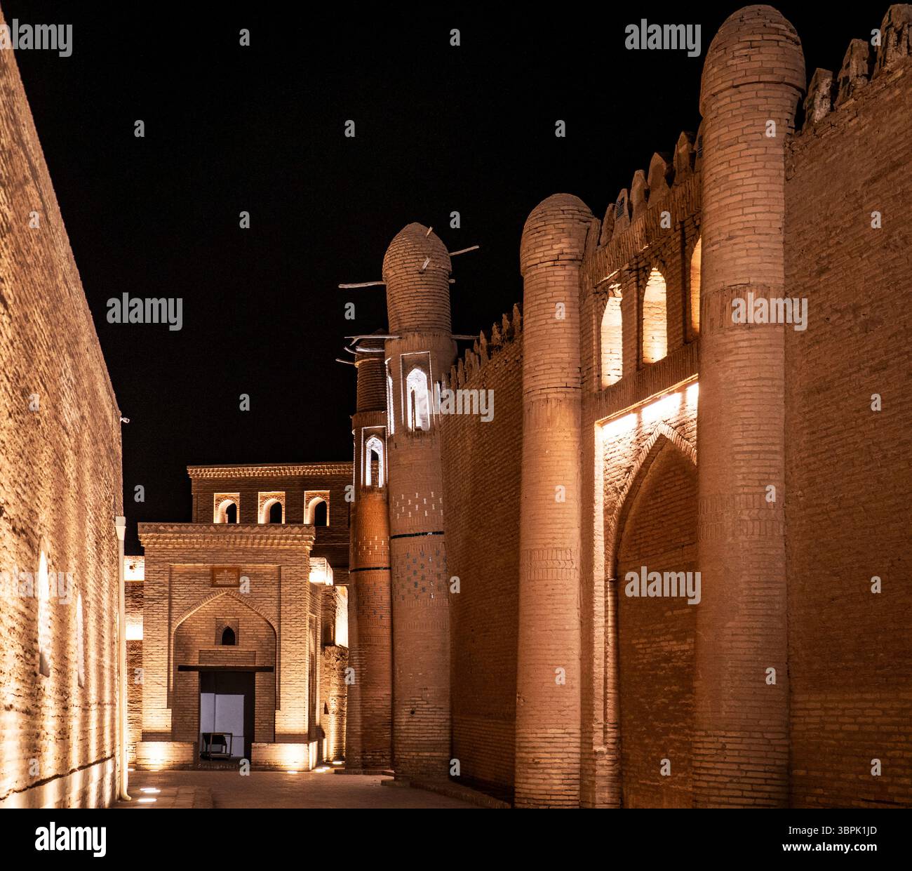 Ein wunderschön beleuchtetes historisches Gebäude bei Nacht, das komplexe Mauerwerk und architektonische Details zeigt. Die Szene erfasst einen schmalen Pfad Stockfoto
