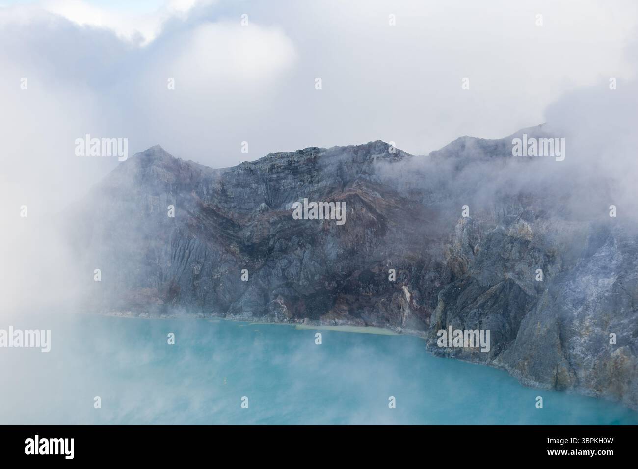 Blick auf das ätherische türkisfarbene Seenwasser trifft auf den zerklüfteten, rauchigen Vulkankrater, der in Nebel gehüllt ist, eine Szene von rauer natürlicher Schönheit, Ijen Volcano Crater, EA Stockfoto