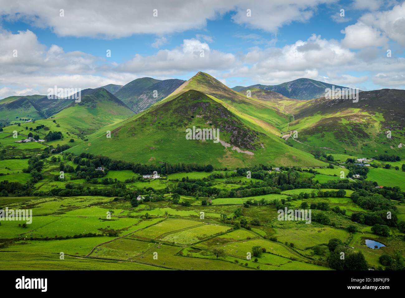 Eine malerische Reihe von Fjells in der Nähe von Catbells im Lake District, mit Bauernhöfen und Bauernhäusern im üppigen grünen Tal an ihrer Basis. Stockfoto