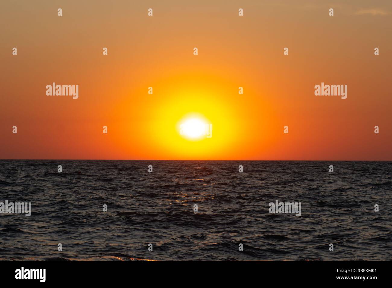 Ein lebhafter Sonnenuntergang über dem Meer mit warmen Farben, die sich auf den sanften Wellen spiegeln Stockfoto