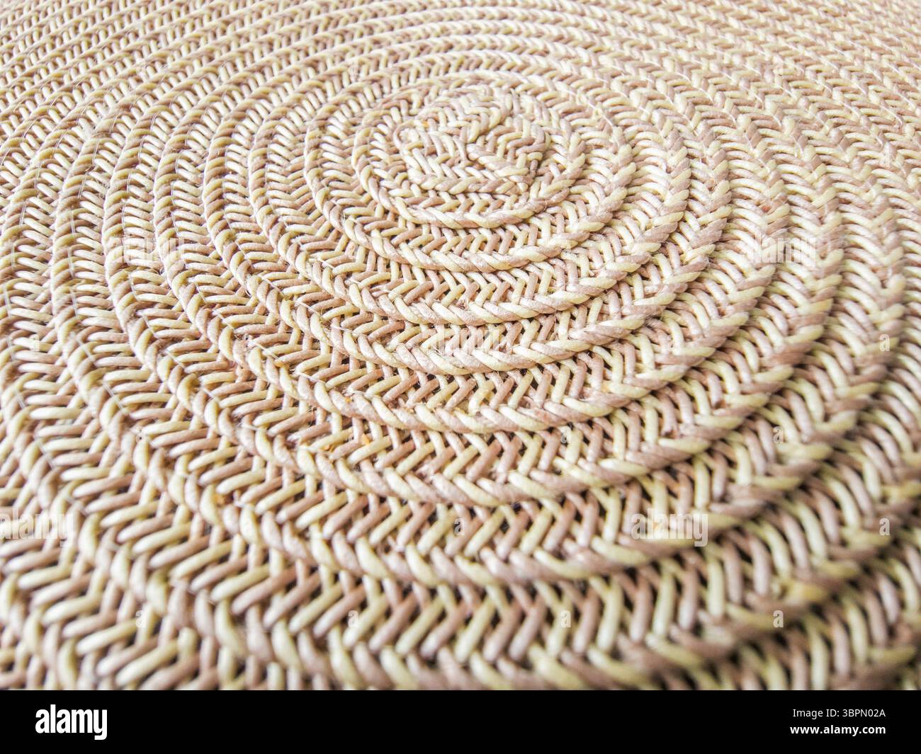 Nahaufnahme einer gewebten runden Matte aus natürlichen Materialien mit detailliertem Spiralmuster. Es ist ideal für die Bereicherung mit ITS Stockfoto