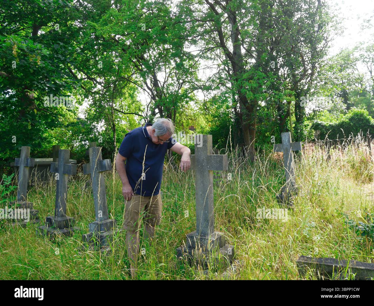 Ein älterer Mann mit geneigtem Kopf, der sich auf einen Grabstein stützt, zum Gedenken an einen geliebten Menschen Stockfoto