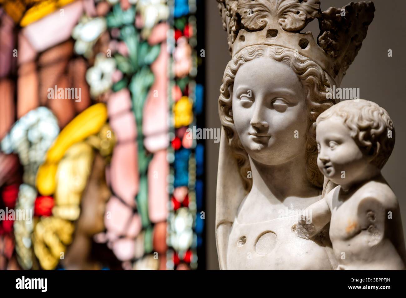 National Gallery of Art Madonna and Child Sculpture Washington DC // WASHINGTON DC – Eine religiöse Skulptur, die die Jungfrau Maria mit dem Christkind zeigt, steht vor einem Buntglasfenster in der National Gallery of Art Das hingebungsvolle Kunstwerk veranschaulicht die traditionelle christliche Ikonographie, wobei Maria als Madonna mit ihrem kleinen Sohn dargestellt wird. Die 1937 gegründete National Gallery of Art beherbergt eine umfangreiche Sammlung religiöser Kunst aus mehreren Jahrhunderten und künstlerischen Bewegungen. Die Sammlung des Museums umfasst zahlreiche Beispiele marianischer Kunst, die die Madonna und widerspiegelt Stockfoto