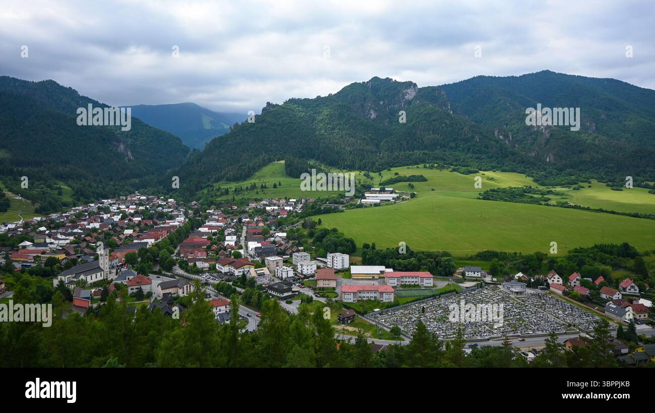 Atemberaubende Aussicht auf eine bezaubernde europäische Stadt, eingebettet in sanfte grüne Hügel und imposante Berge, die eine ruhige und idyllische Szene schaffen. Stockfoto