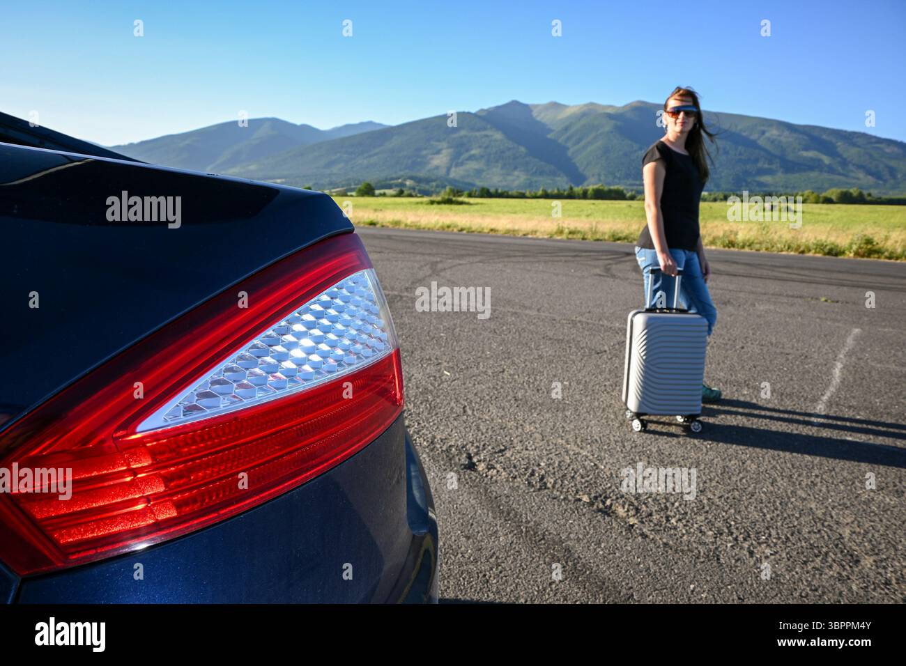 Touristen, die an ihrem Ziel ankommen, gehen auf einer Bergstraße mit ihrem Trolley und lassen ihr Auto zurück. Stockfoto
